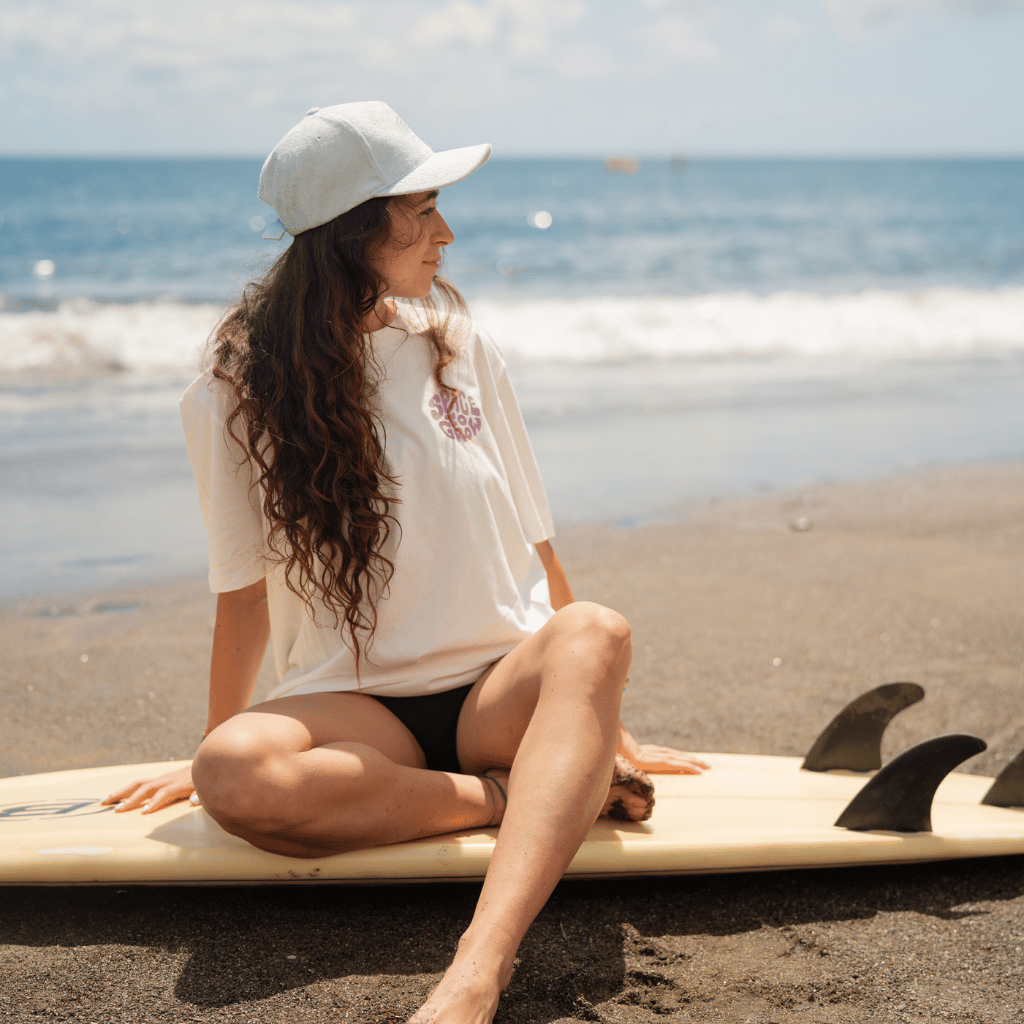 Frottee Cap - Fresh Mint mit Ton-in-Ton Stickerei, getragen von einer Frau sitzend auf einem Surfbrett am Strand, seitlich fotografiert mit Meer im Hintergrund