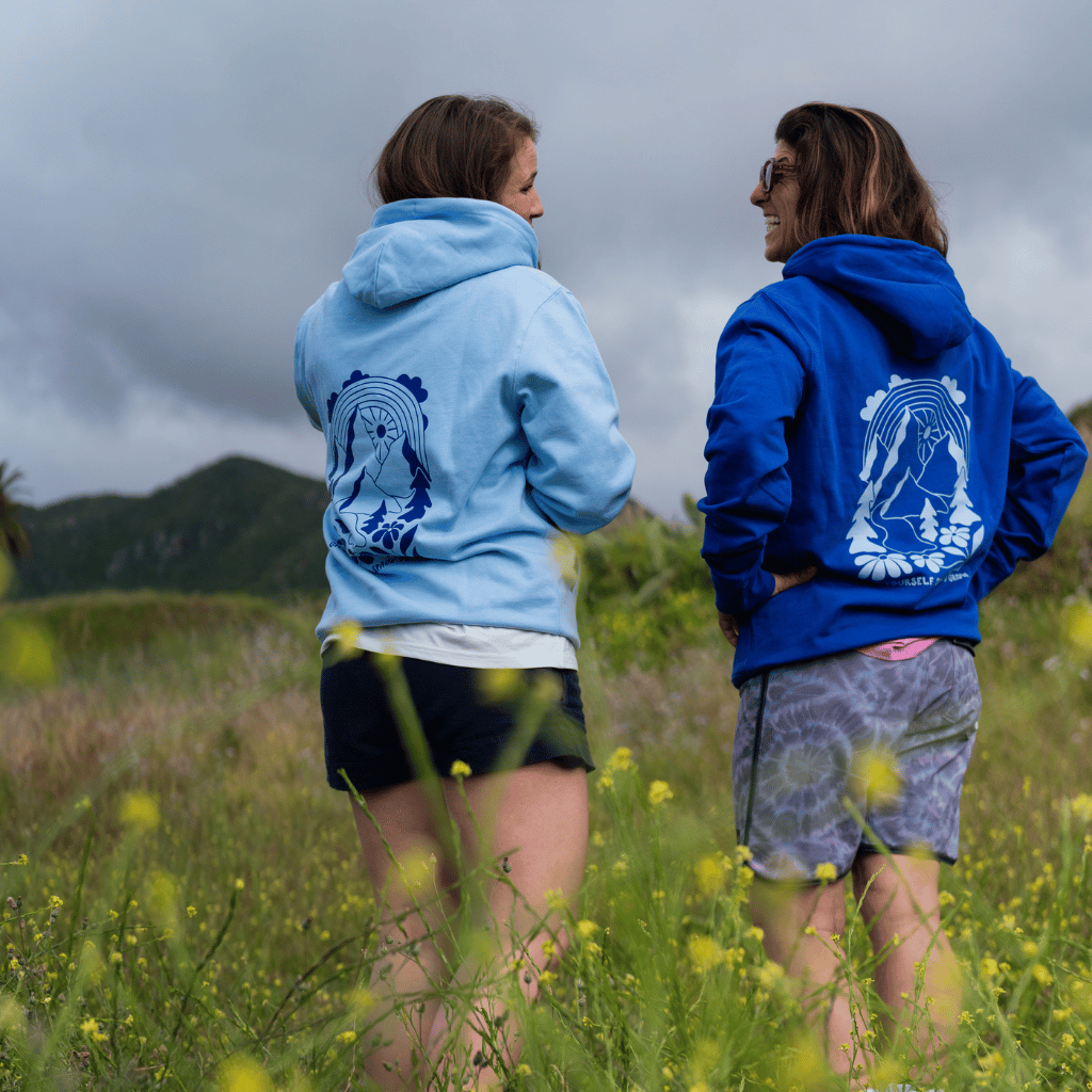 Space to Grow Mountain - Unisex Pullover mit großem Rückenprint in Hellblau und Dunkelblau, getragen von zwei Frauen in einem Feld mit Bergen im Hintergrund.