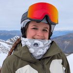 Printed Neckwarmer - Fluffy Grey Leo mit WESORA-Patch, getragen von Skifahrer auf verschneitem Berg, mit Salomon-Helm und gemustertem Skijacke, seitliche Ansicht.