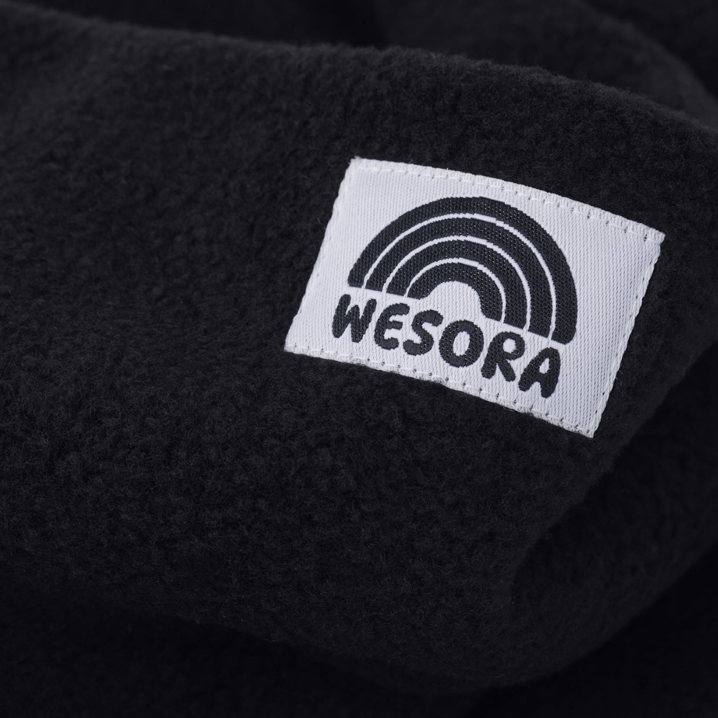 Eltern + Kind Bundle - Fleece Neckwarmer All Black mit weichem Fleece und kleinem Label „WESORA“ mit Regenbogengrafik, Nahaufnahme des Stoffes.