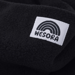 Eltern + Kind Bundle - Fleece Neckwarmer All Black mit weichem Fleece und kleinem Label „WESORA“ mit Regenbogengrafik, Nahaufnahme des Stoffes.