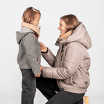 Eltern + Kind Bundle - Fleece Neckwarmer The Teddy, getragen von einer Frau und einem Mädchen, die sich lächelnd helfen, den Neckwarmer anzupassen.