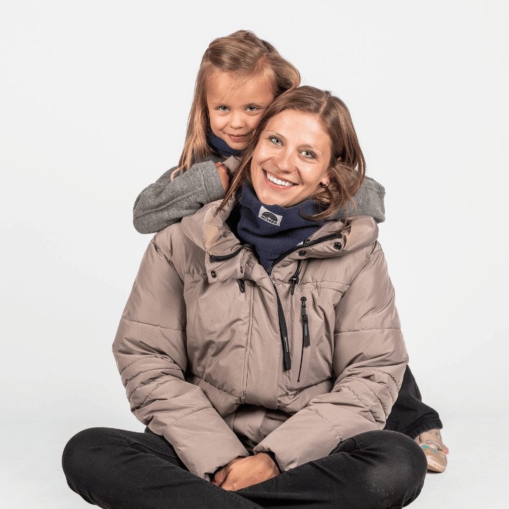 Eltern + Kind Bundle - Fleece Neckwarmer Midnight Blue, getragen von einer lächelnden Frau mit Kind, in entspannter Pose vor weißem Hintergrund.