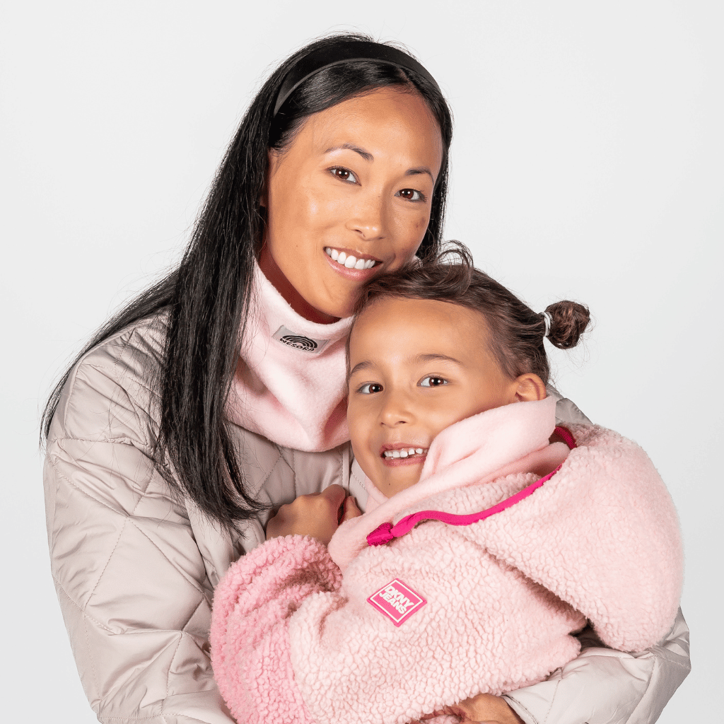 Eltern + Kind Bundle - Fleece Neckwarmer Candy Rose, getragen von einer Frau und einem Kind in winterlichen Jacken, lächelnd und umarmend vor neutralem Hintergrund.