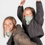 Eltern + Kind Bundle - Fleece Neckwarmer Fresh Mint, getragen von einer lächelnden Frau mit spielendem Kind im Arm, fotografiert vor weißem Hintergrund.