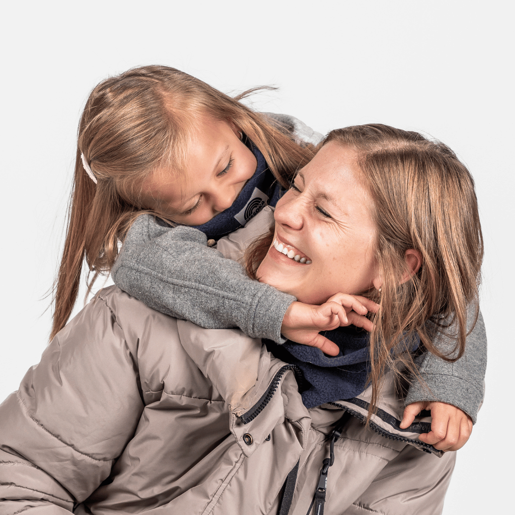 Eltern + Kind Bundle - Fleece Neckwarmer Midnight Blue, getragen von Frau und Mädchen, die lächelnd posieren, fotografiert in einem warmen, hellen Hintergrund.