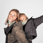 Eltern + Kind Bundle - Fleece Neckwarmer Fresh Mint, getragen von einer lachenden Frau in einem shearlinggefütterten Mantel und einem Kind auf ihrem Rücken, beide fröhlich posierend.