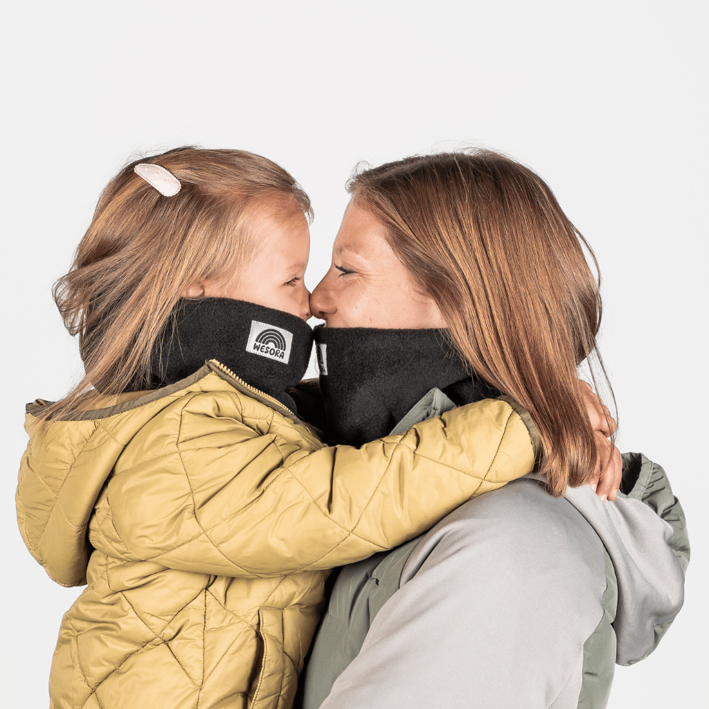 Eltern + Kind Bundle - Fleece Neckwarmer All Black, getragen von Frau und Kind in warmer Umarmung, beide lächeln und tragen passende schwarze Halswärmer mit Wesora-Logo.