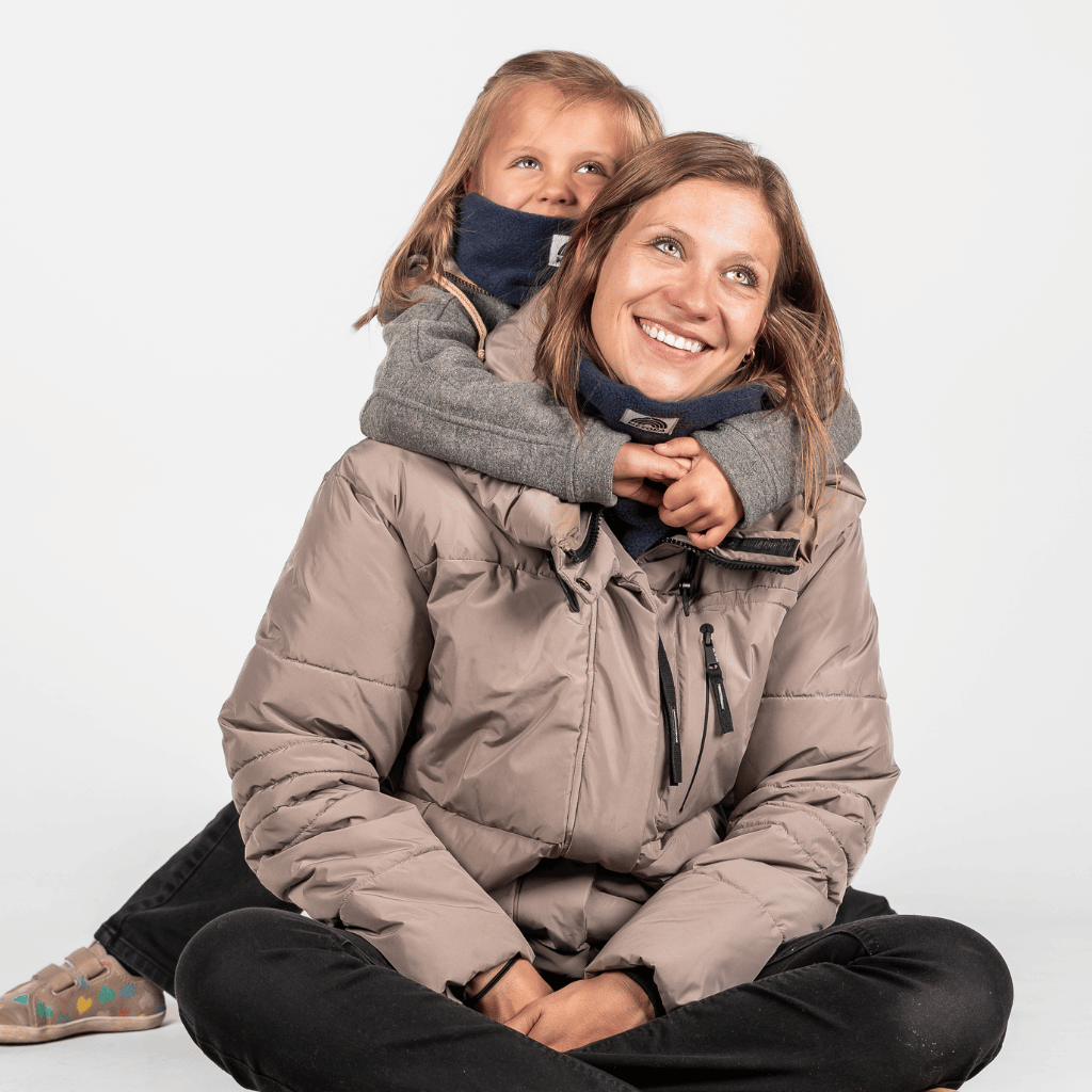 Eltern + Kind Bundle - Fleece Neckwarmer Midnight Blue, getragen von einem Kind, das eine Frau umarmt, beide lächelnd und leicht nach rechts schauend.