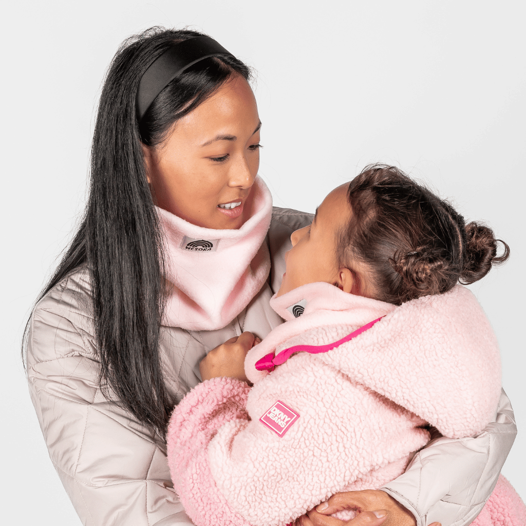Eltern + Kind Bundle - Fleece Neckwarmer Candy Rose, getragen von Frau und Kind in warmen, rosa Fleece, einander zugewandt, vor hellem Hintergrund.