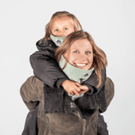 Eltern + Kind Bundle - Fleece Neckwarmer Fresh Mint, getragen von einer Frau mit Kind auf dem Rücken, beide lächelnd in Winterjacken.