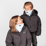 Eltern + Kind Bundle - Fleece Neckwarmer Baby Blue, getragen von Frau und Kind in schwarzen Winterjacken, lächelnd zueinander schauend, vor hellem Hintergrund.