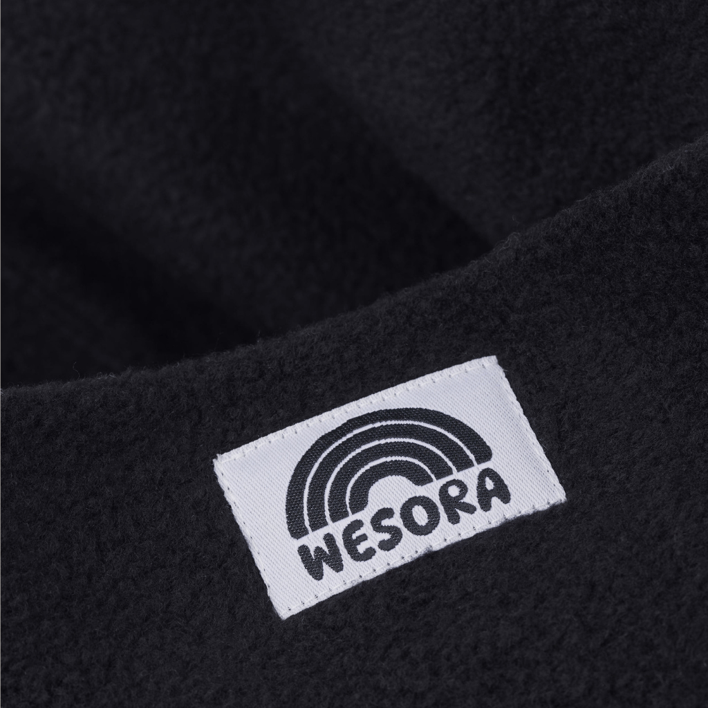 Fleece Neckwarmer -All Black Kid mit WESORA-Label, Nahaufnahme des weichen, schwarzen Stoffes, ideal für Abenteuer und Wärme.