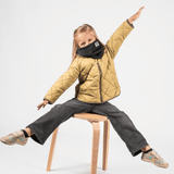 Fleece Neckwarmer -All Black Kid, getragen von einem spielenden Kind auf einem Holzstuhl, mit ausgestreckten Armen, spielerisch und dynamisch in Bewegung.