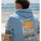 All comes in Waves - Unisex Pullover mit maritimem Design, getragen von einem Mann am Strand, der auf einer Bank mit Surfbrett sitzt.