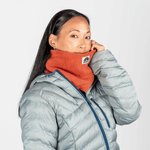 Fleece Neckwarmer - Autumn Nectar in leuchtendem Orange mit Regenbogen-Logo, getragen von Person mit grauer Jacke, vor hellem Hintergrund.