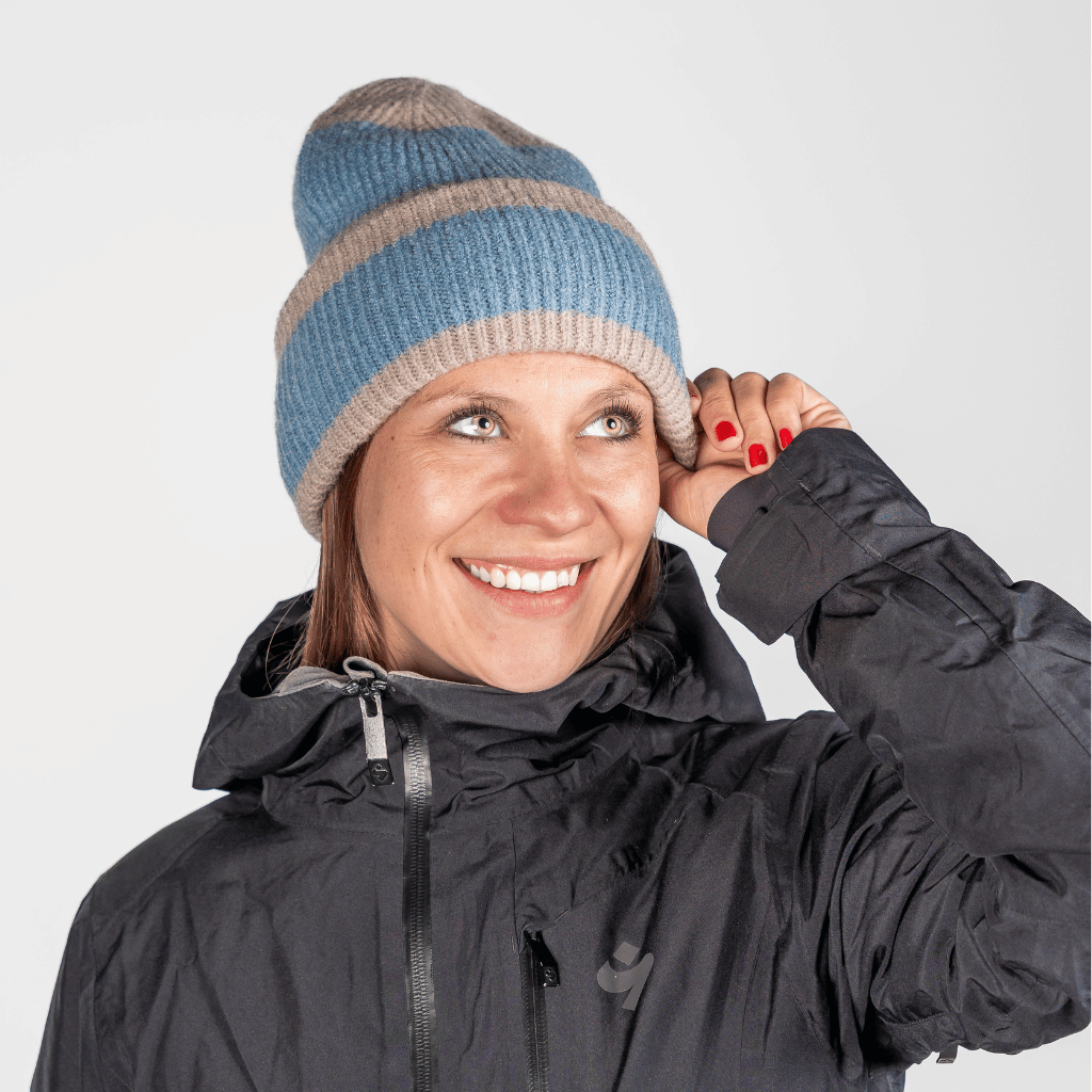 Beanie - Blue Lagon Twist mit gestreiftem Strickdesign, getragen von lächelnder Frau in Winterjacke, die den Rand der Mütze anpasst.