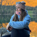 Beanie - Peach Fuzz mit doppellagigem Strickdesign, getragen von einer Frau am See bei Sonnenuntergang, sitzt auf einem Felsen.