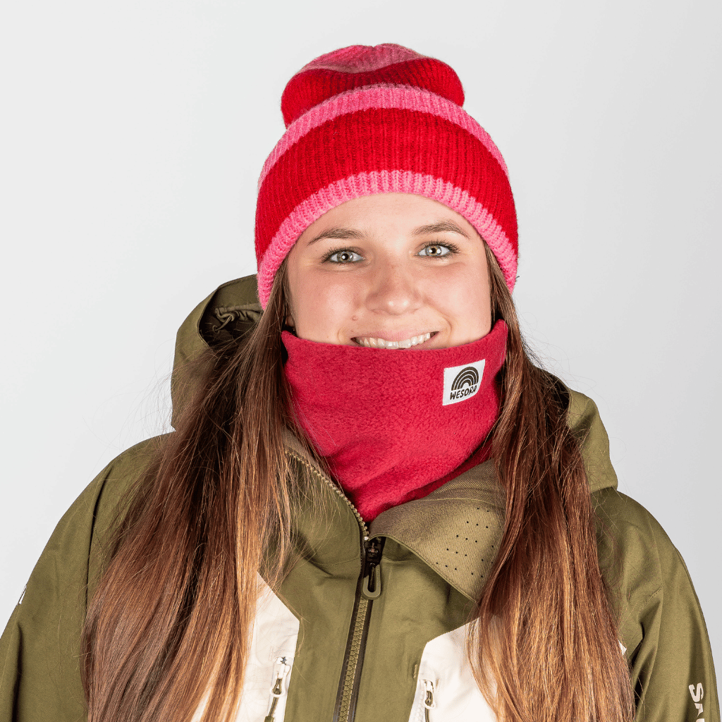 Beanie - Pink Berry Twist mit rot-pinken Streifen, getragen von Person mit langem braunem Haar, lächelnd in Winterkleidung, Nahaufnahme.