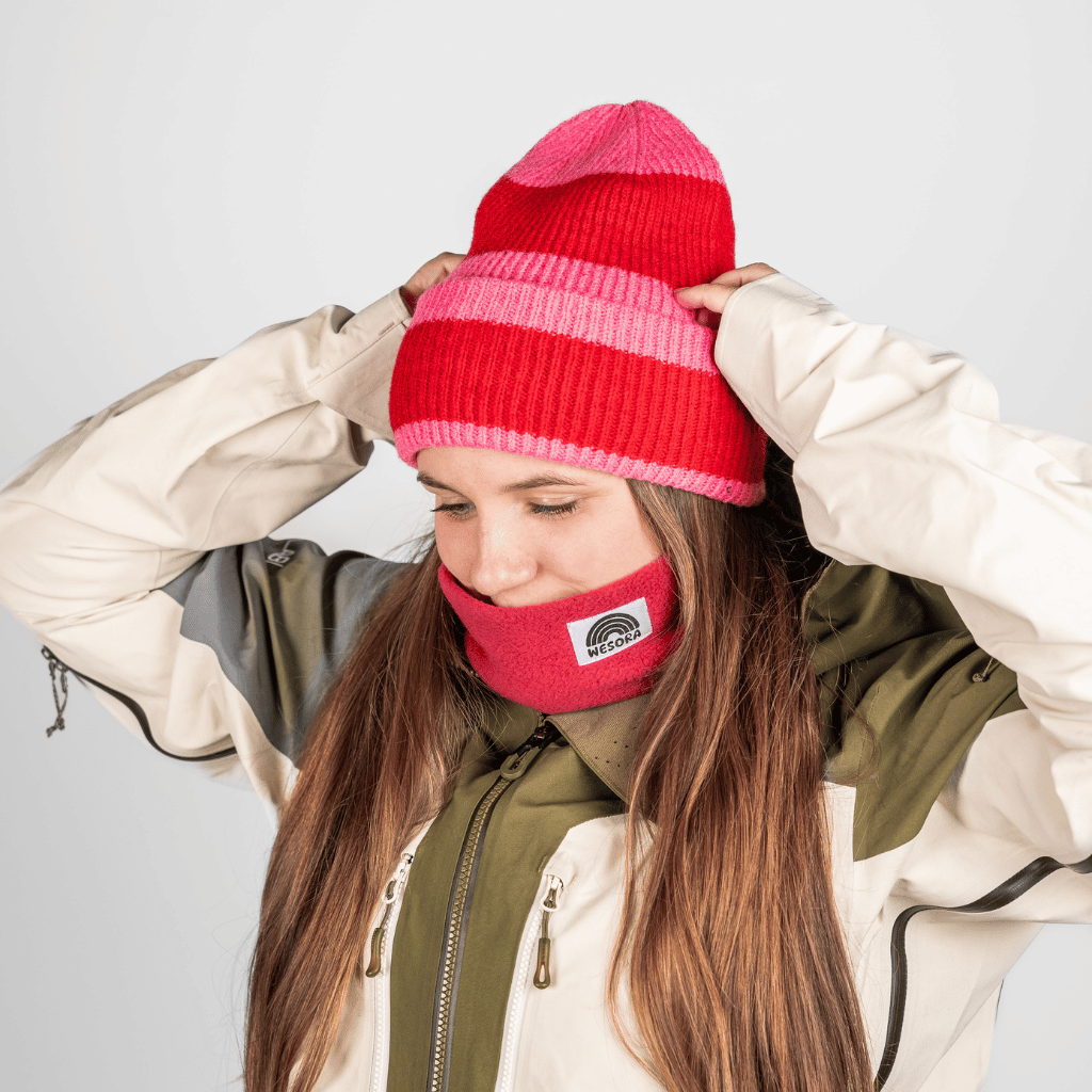Beanie - Pink Berry Twist mit gestreiftem Design, getragen von Person mit langem Haar, passend zum roten Fleece-Nackenwärmer und zweifarbiger Jacke.