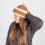 Beanie - Toffee Twist mit gestreiftem Strickdesign, getragen von einer Frau in Profilansicht, die den hinteren Teil der Mütze anpasst.