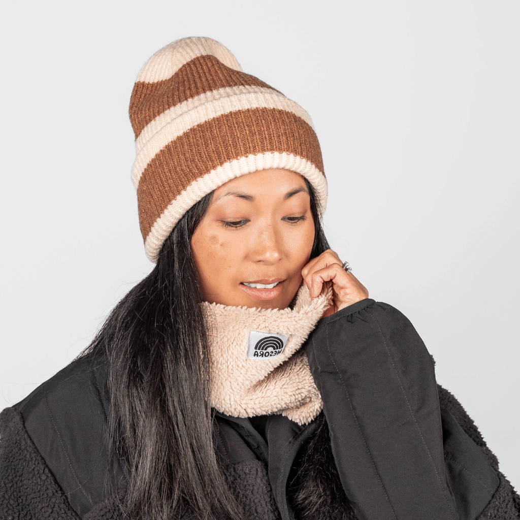 Beanie - Toffee Twist mit geripptem Strickdesign und warmem Toffee-Creme-Muster, getragen von einer Frau, die den Neckwarmer anpasst, im Studio fotografiert.