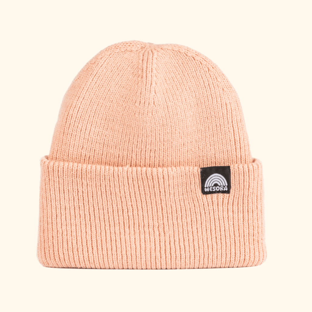 Beanie - Peach Fuzz mit geripptem Strickdesign und breitem Umschlag, WESORA-Logo auf schwarzem Etikett, gefaltet.