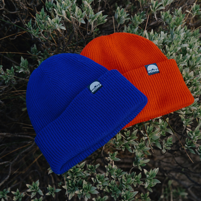 Beanie - Sunset Red mit doppellagigem, geripptem Strickdesign und breitem Umschlag, Nahaufnahme zeigt das nachhaltige Material aus recyceltem Polyester, liegend auf einem Busch, Nahaufnahme.