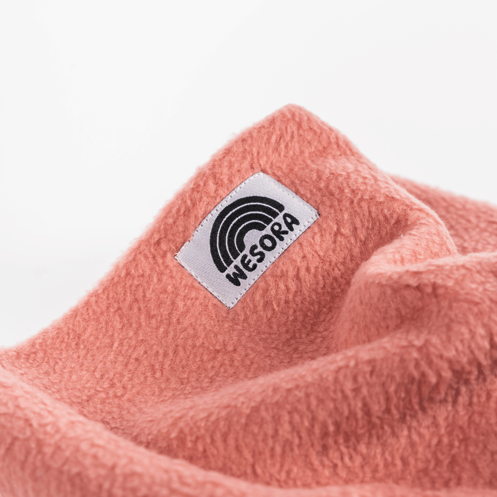 Fleece Neckwarmer - Berry Blossom Kid mit weichem, korallenrosa Stoff und weißem Etikett mit Regenbogengrafik und WESORA-Markenname.