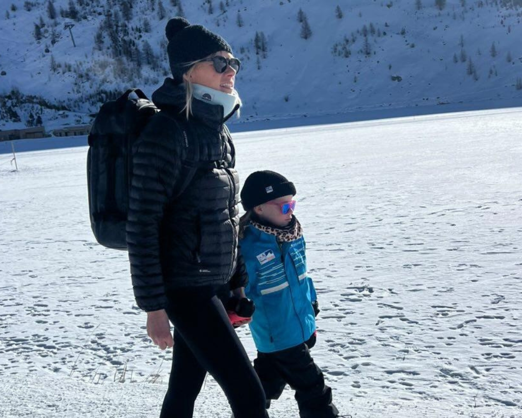 Eine Mutter und ihr Kind tragen einen Neckwarmer (Baby Blue und Classic Leo). Die beiden wandern gemeinsam durch die Schneelandschaft.
