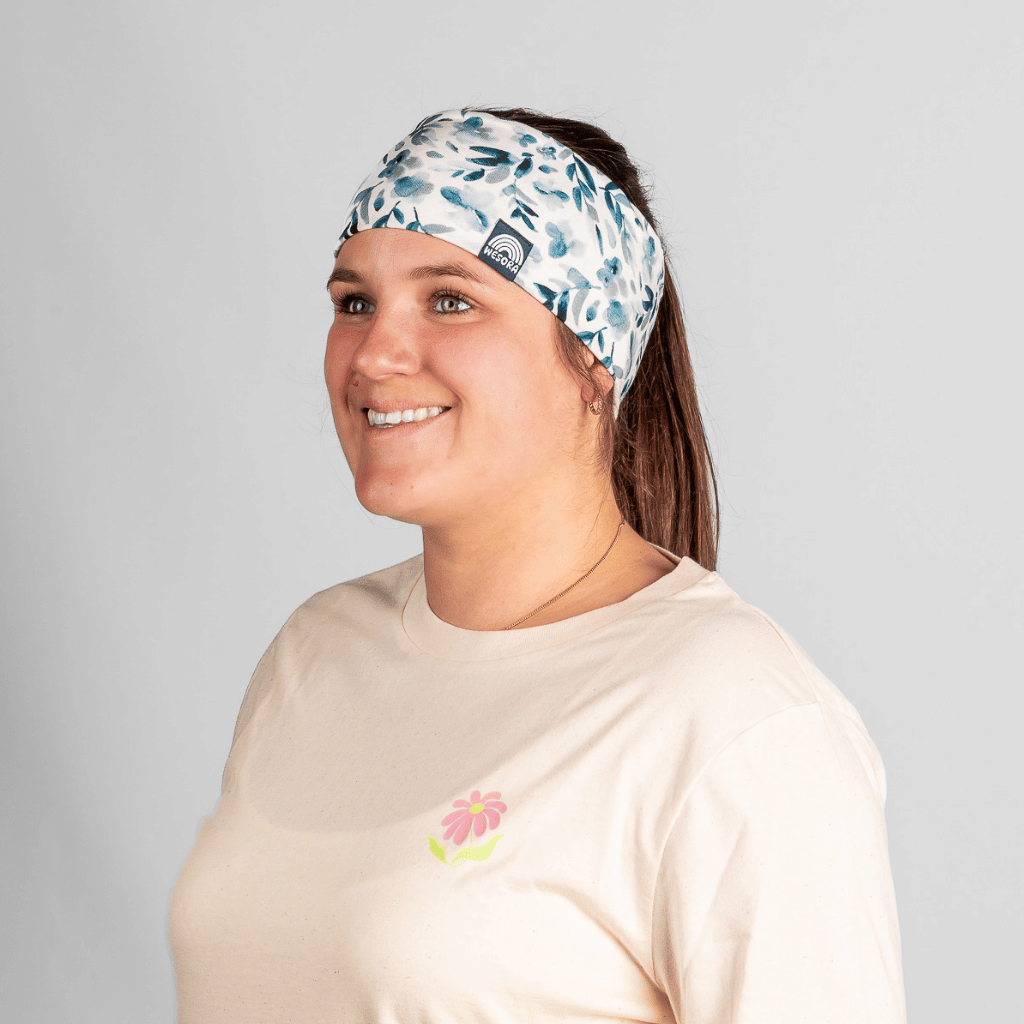 Stirnband - Blue Blossom mit floralem Design, getragen von lächelnder Frau in beige T-Shirt, seitlich fotografiert.