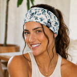 Stirnband - Blue Blossom mit blauen Blumen, getragen von einer lächelnden Frau mit braunen Haaren in lockerem Zopf, Nahaufnahme.