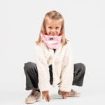 Fleece Neckwarmer - Candy Rose Kid, getragen von einem lächelnden Mädchen in flauschiger Jacke und dunklen Hosen, fotografiert vor weißem Hintergrund in Hocke.