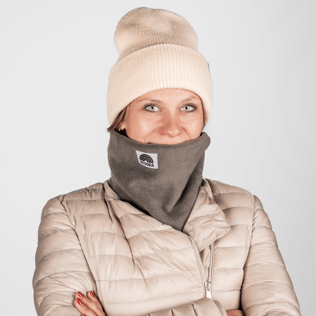 Fleece Neckwarmer - Cloudy Grey, getragen von einer Person mit verschränkten Armen, zeigt nur Augen und Nasenrücken, in einer neutralen Umgebung.