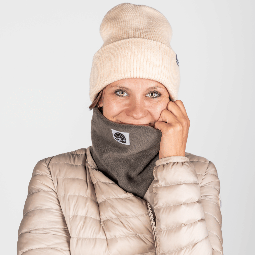 Fleece Neckwarmer - Cloudy Grey, getragen von einer jungen Frau in Winterkleidung, mit NESORA-Logo sichtbar, lässig und elegant für Outdoor-Abenteuer.
