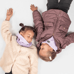 Fleece Neckwarmer - Dreamy Lilac Kid, getragen von fröhlichem Kind, fotografiert von oben, liegend auf Boden, ideal für Winterabenteuer und Wärme beim Spielen.