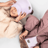 Fleece Neckwarmer - Dreamy Lilac Kid mit kuscheligem Design, getragen von zwei lächelnden Kindern in WESORA-Beanies, liegend auf einer hellen Oberfläche.