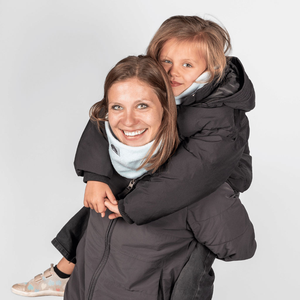Eltern + Kind Bundle - Fleece Neckwarmer Baby Blue, getragen von Frau und Kind im Winterlook, fotografiert vor einem grauen Hintergrund, beide lächelnd und warm eingepackt.
