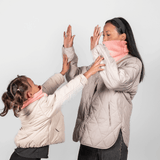 Eltern + Kind Bundle - Fleece Neckwarmer Peachy Rose, getragen von Mutter und Tochter in einem spielerischen Moment, beide mit beige Steppjacken, Hände zum High-Five erhoben.