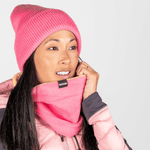 Fleece Neckwarmer - Skisister Edition 2 mit SKISISTERS-Label, getragen von Frau mit dunklem Haar, zieht ihn über Gesicht, fotografiert vor grauem Hintergrund.