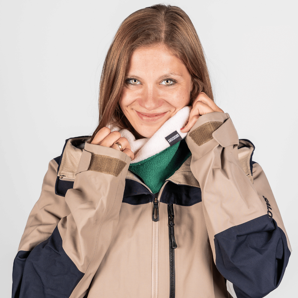 Fleece Neckwarmer - Skisister Edition 1 mit kleinem Stoffetikett, getragen von einer lächelnden Frau, fotografiert vor einem neutralen Hintergrund.