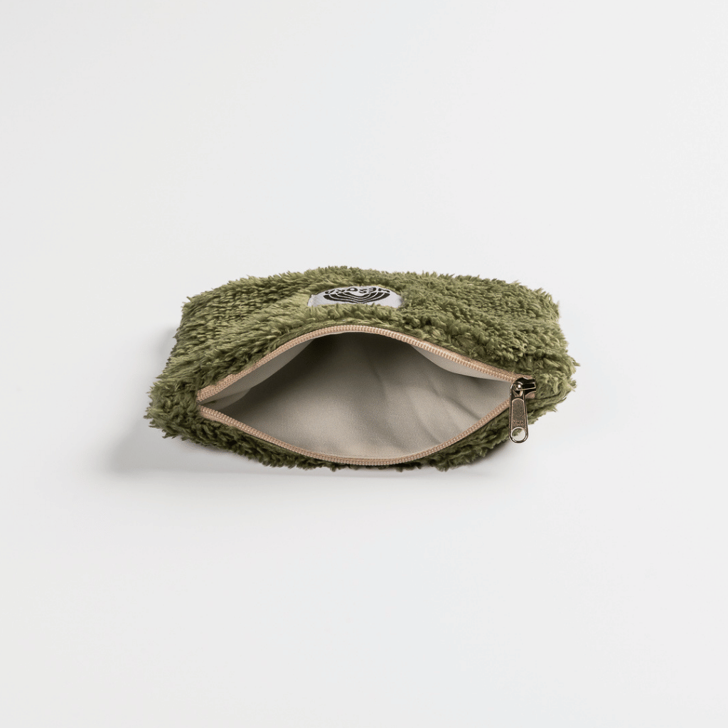 Fluffy Zip Bag - Dunkelgrün mit olivgrünem Kunstfell und schwarzem Grafik-Patch, auf weißem Hintergrund liegend, zeigt einen offenen Reißverschluss mit beigem Innenfutter.