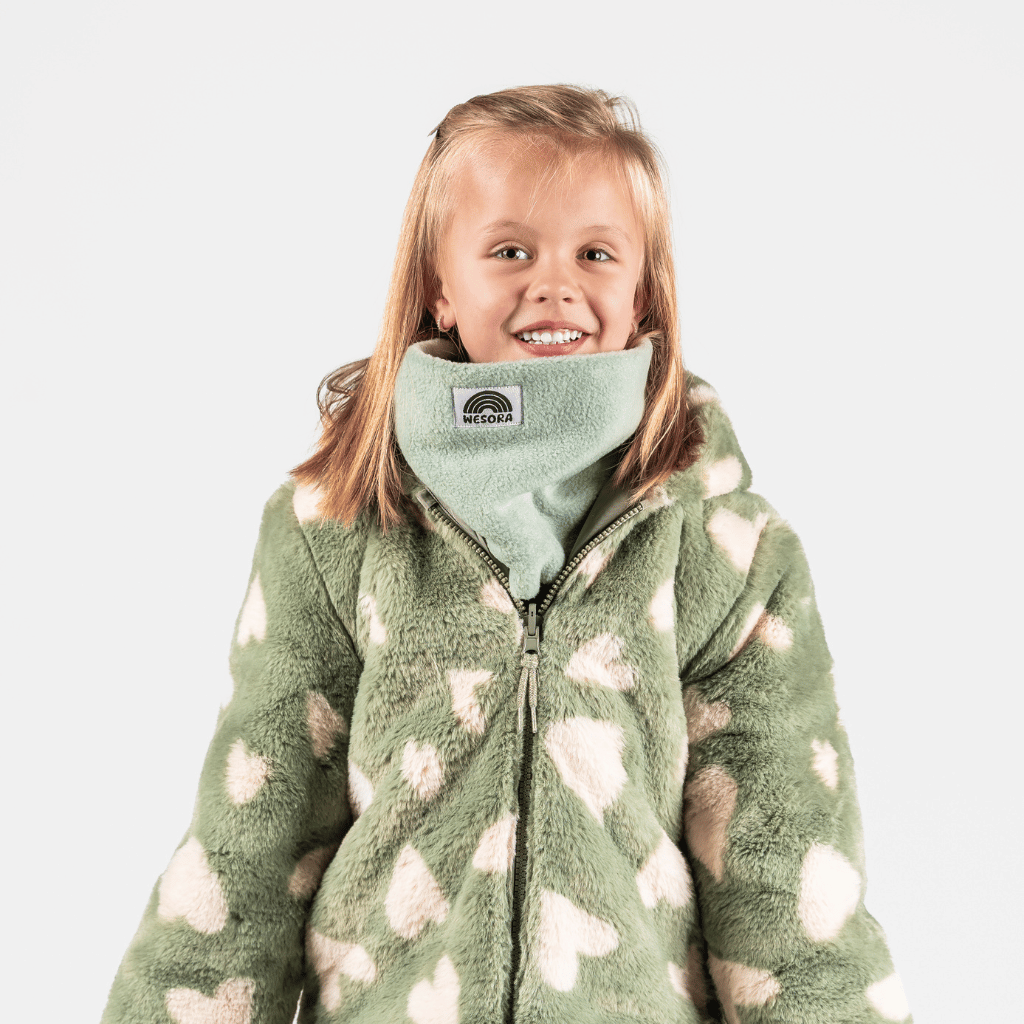 Fleece Neckwarmer - Dreamy Lilac Kid mit Herzmuster, getragen von einem lächelnden Mädchen, fotografiert vor neutralem Hintergrund, ideal für winterliche Abenteuer.