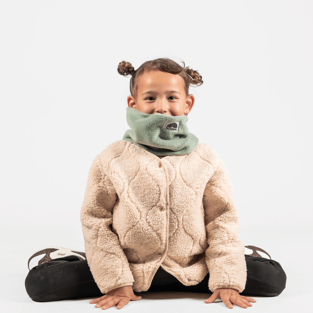 Fleece Neckwarmer - Dreamy Lilac Kid, getragen von einem sitzenden Kind mit neutralem Gesichtsausdruck, zeigt einen weichen, komfortablen Stil für winterliche Abenteuer.