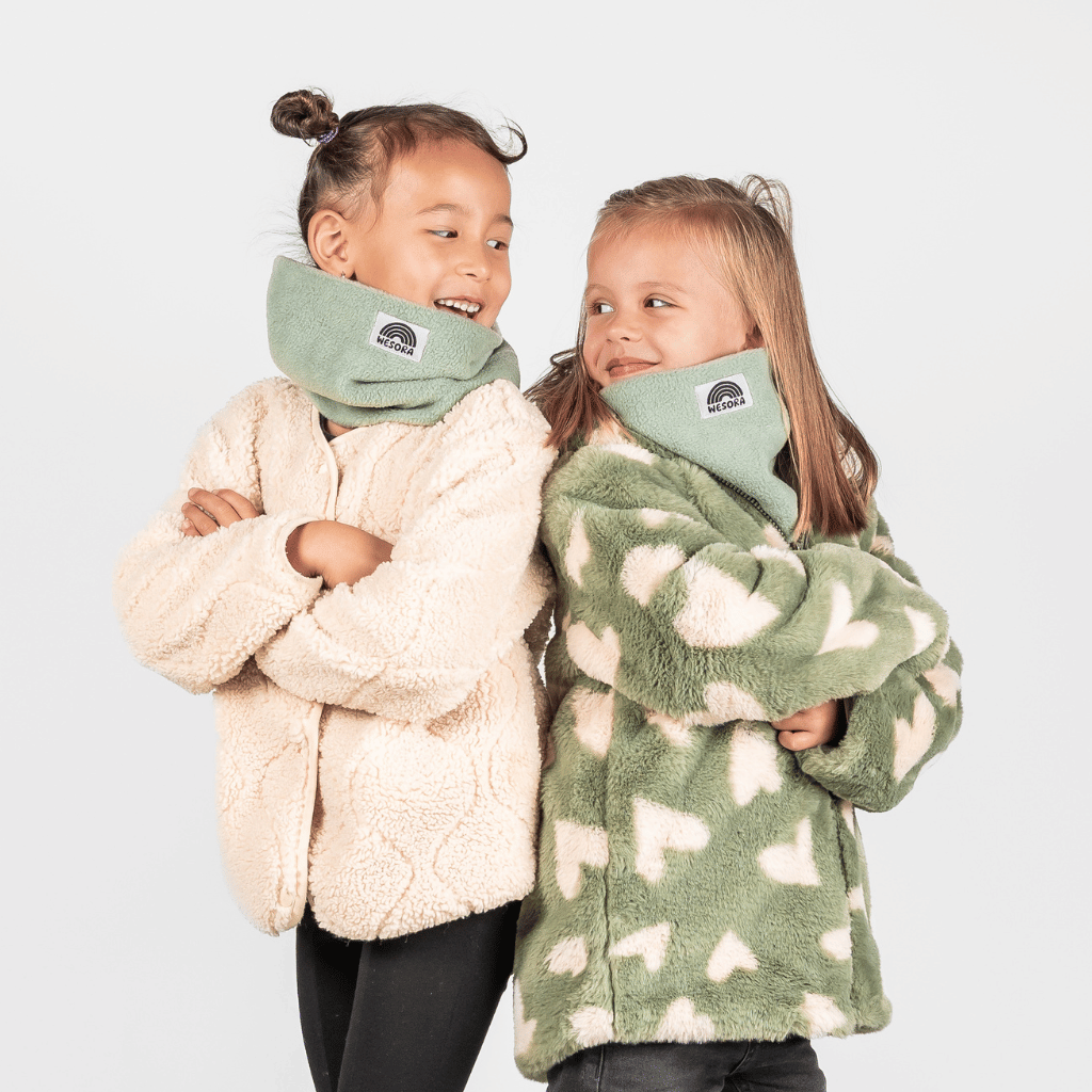 Fleece Neckwarmer - Dreamy Lilac Kid, getragen von zwei lächelnden Kindern in flauschigen Jacken, fotografiert vor einem schlichten Hintergrund, seitlich stehend.