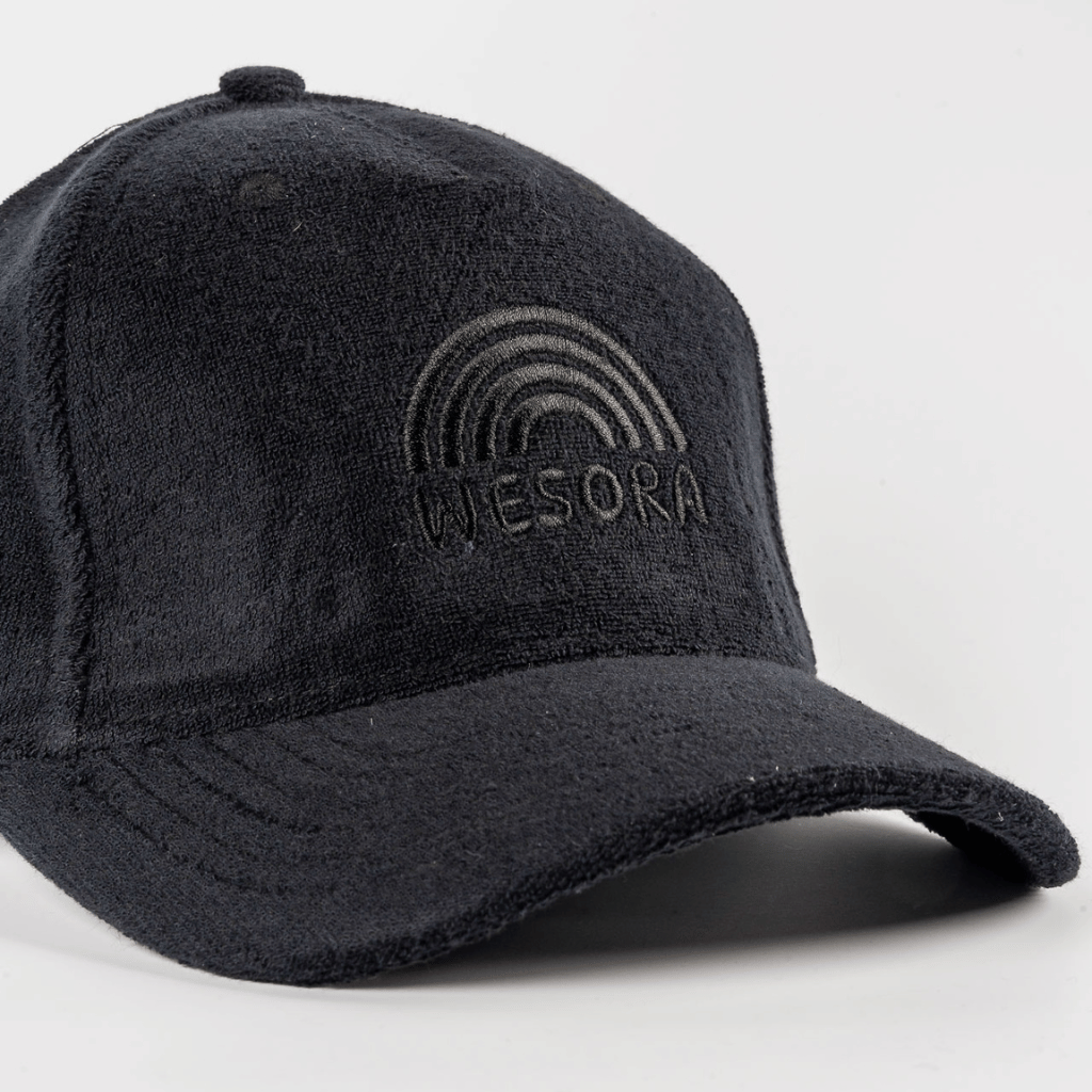 Frottee Cap - All Black mit Ton-in-Ton Regenbogenstickerei über WESORA, aus Frottee-Material, fotografiert in Nahaufnahme, zeigt minimalistisches Design und verstellbaren Klettverschluss.