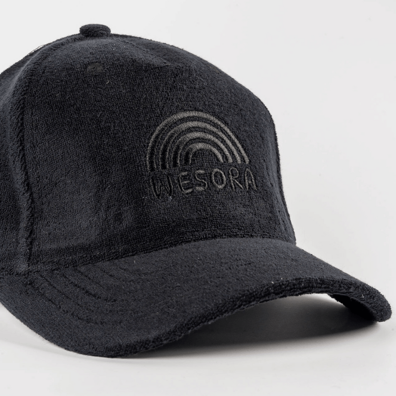 Frottee Cap - All Black mit Ton-in-Ton Regenbogenstickerei über WESORA, aus Frottee-Material, fotografiert in Nahaufnahme, zeigt minimalistisches Design und verstellbaren Klettverschluss.