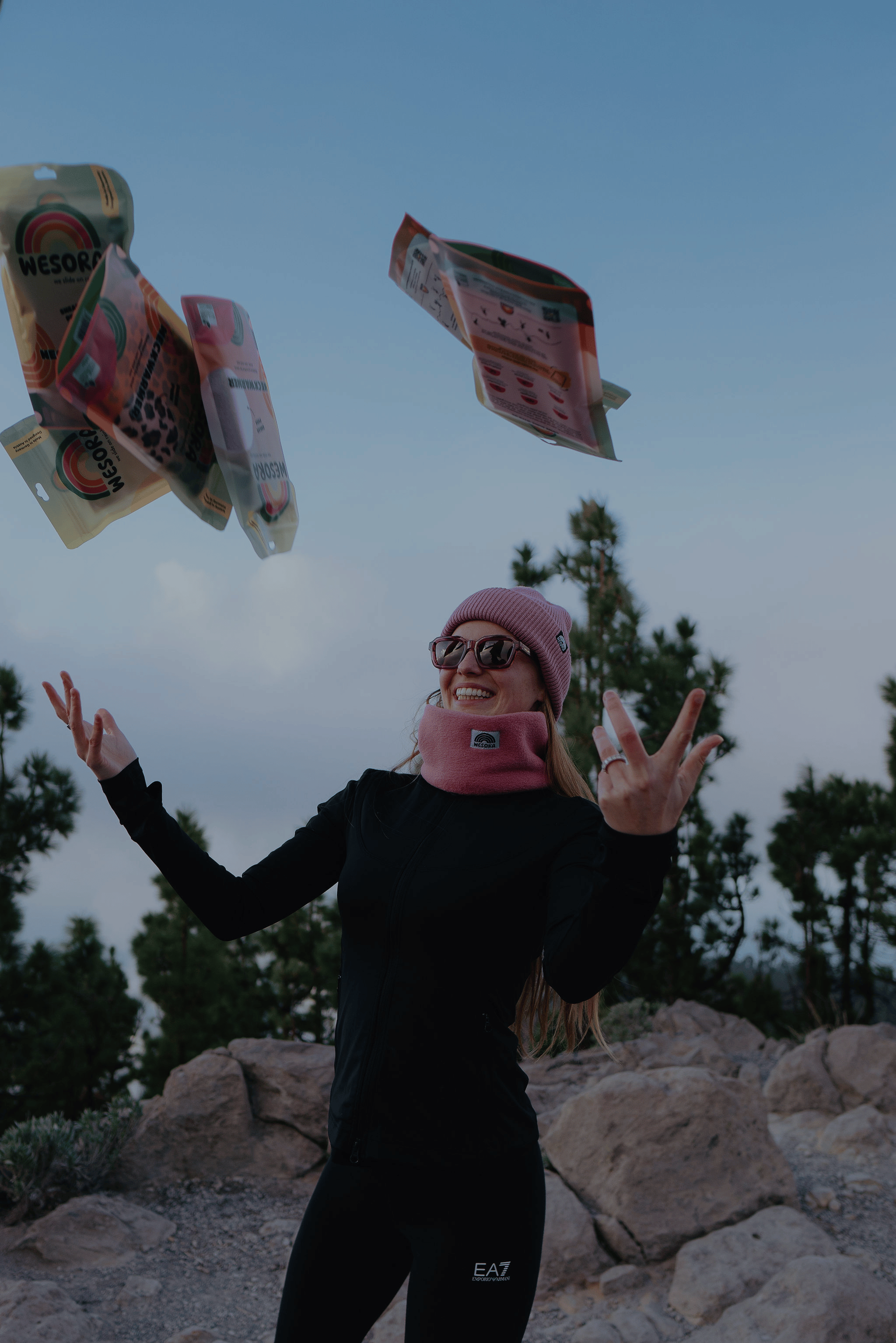 Frau mit breitem Lächeln schmeißt mehrere Neckwarmer in die Luft.