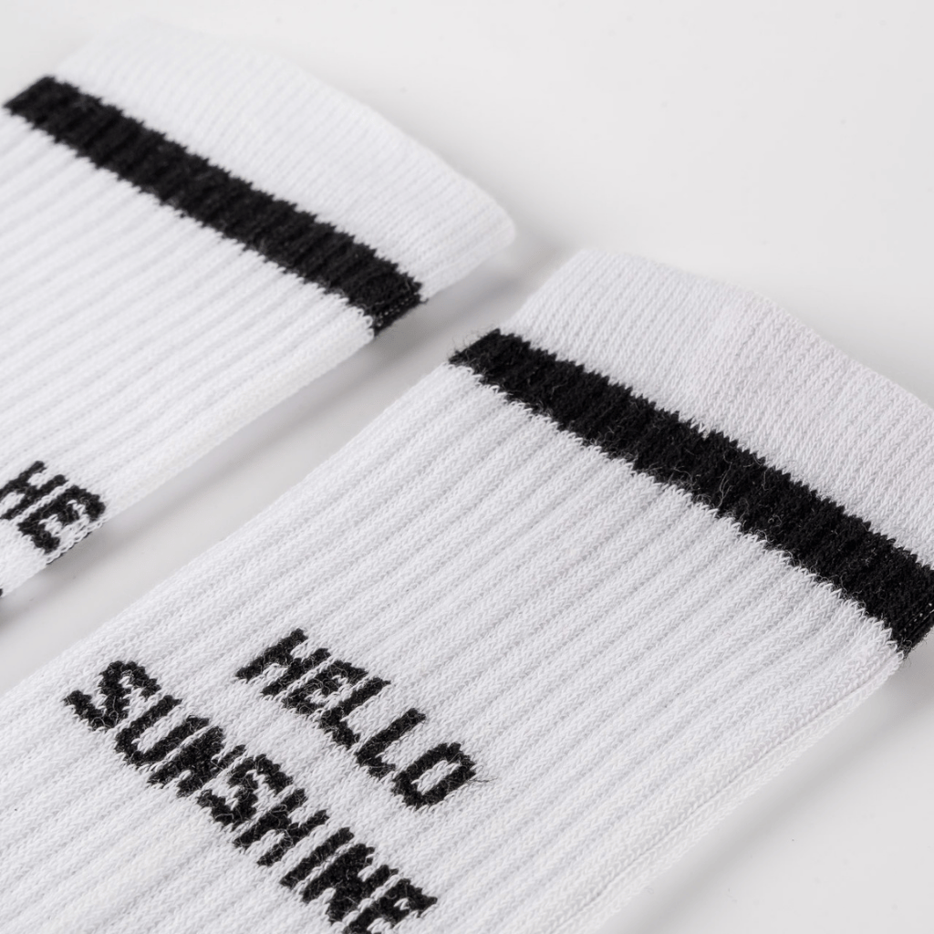 Socken - Hello Sunshine mit schwarzem Streifen am Bündchen und Hello Sunshine-Slogan auf dem Fuß, flach liegend auf hellem Hintergrund.