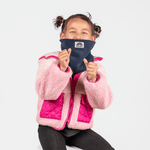 Fleece Neckwarmer -Midnight Blue Kid mit kleinem Logo, getragen von einem lächelnden Kind in pinker Jacke, die Fäuste spielerisch erhoben.